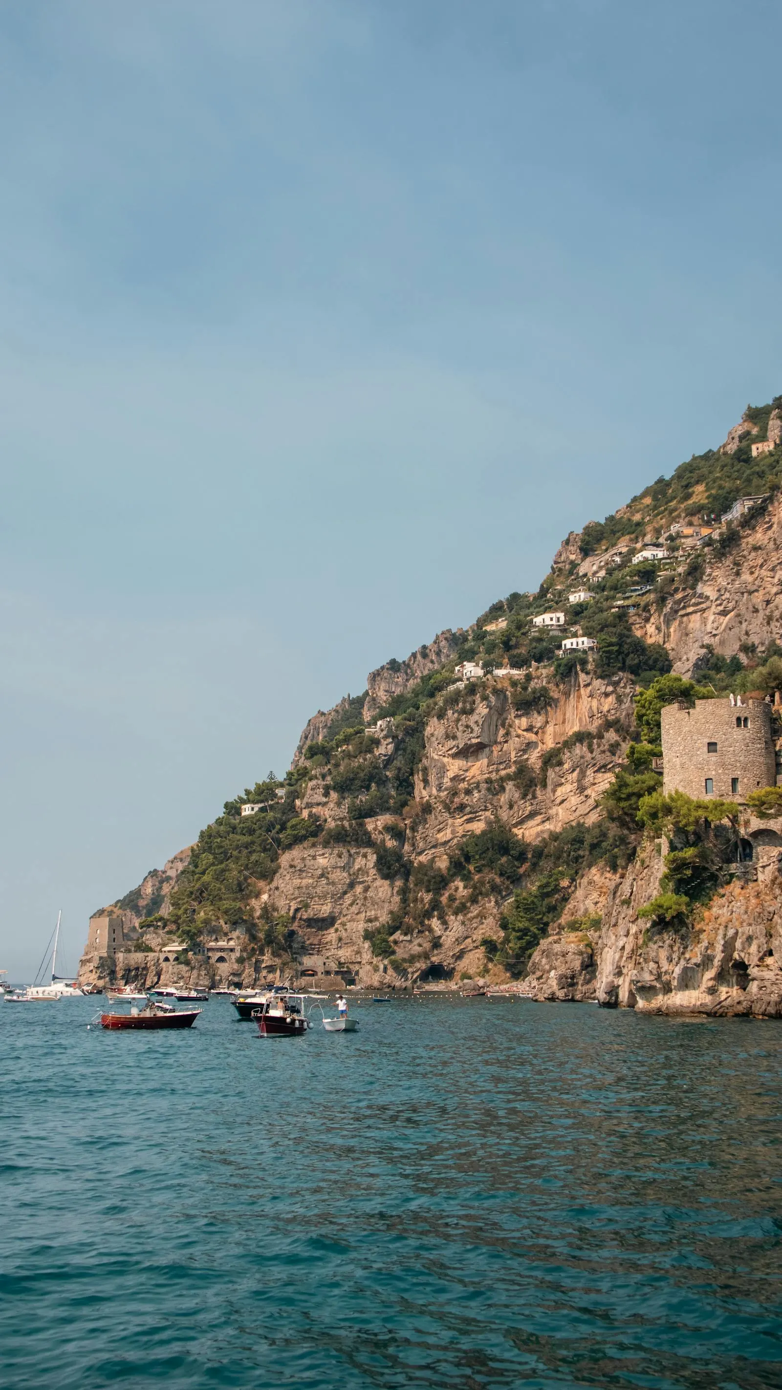 Small boats moored on calm water below a hillside village