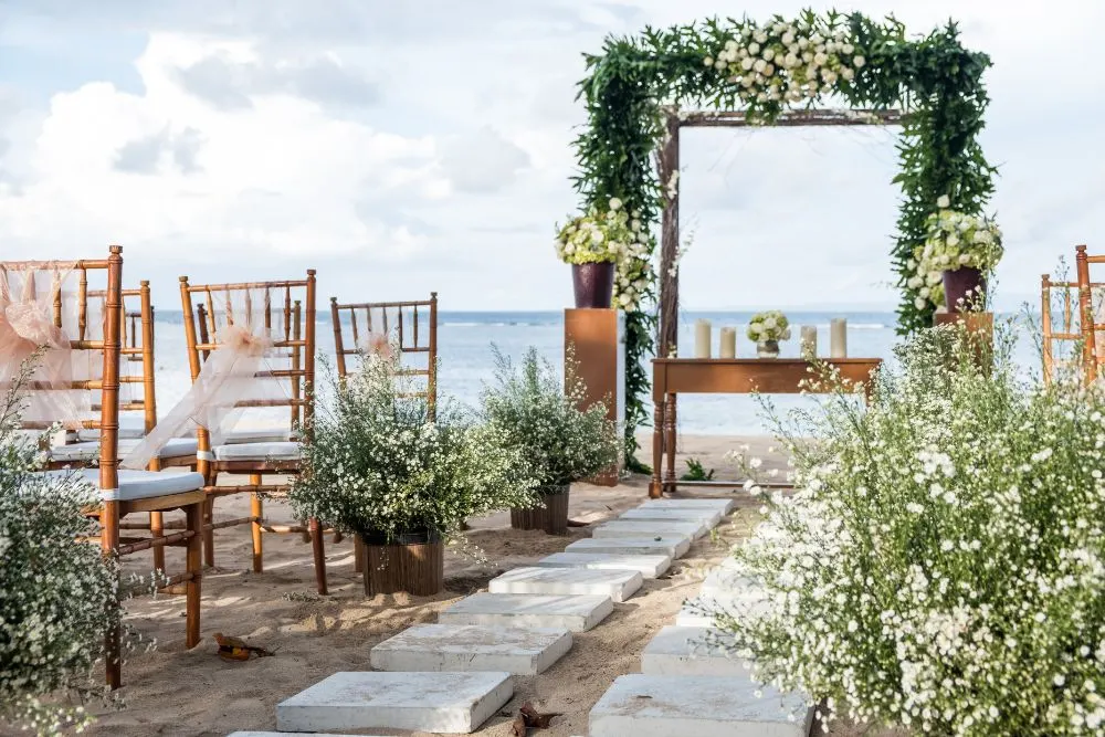 Beachfront wedding ceremony setup with white florals at golden hour