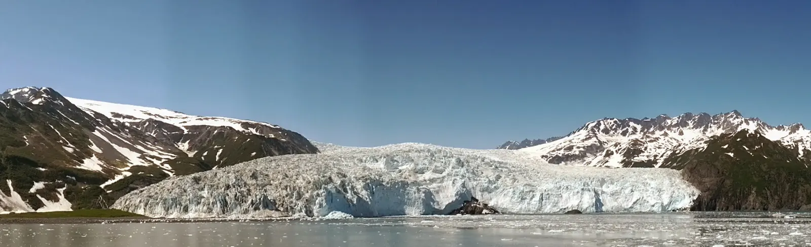 A tidewater glacier meeting the sea beneath snow-covered peaks in Alaska