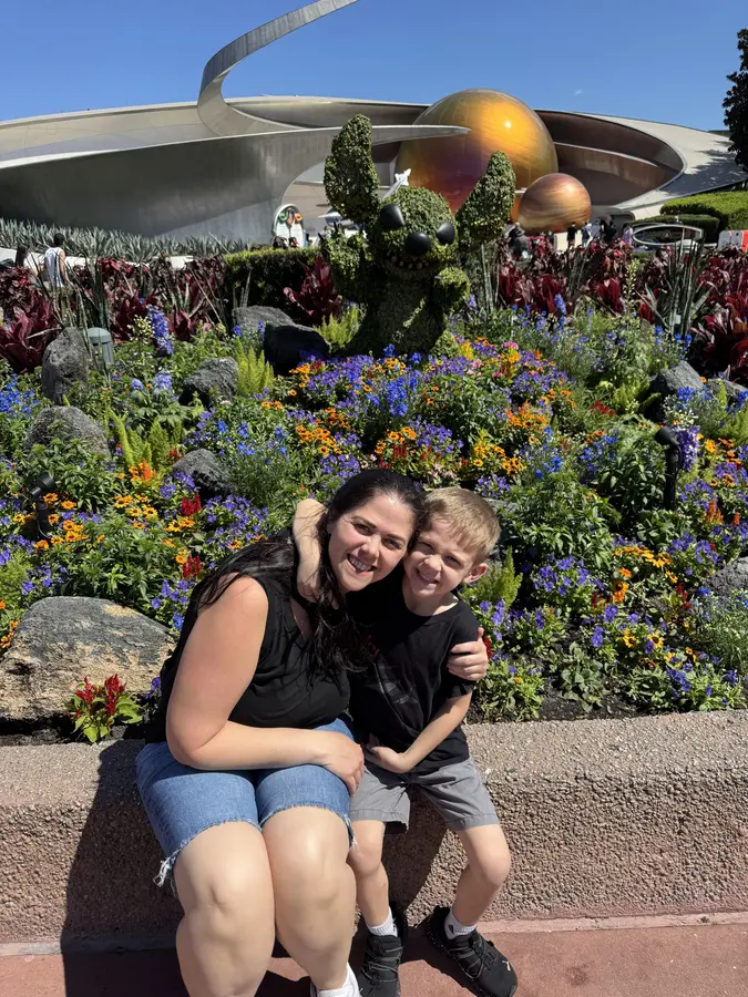 A mom and her son hugging beside an EPCOT flower bed