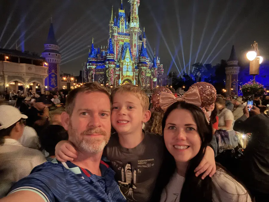 A family smiling in front of the lit Cinderella Castle