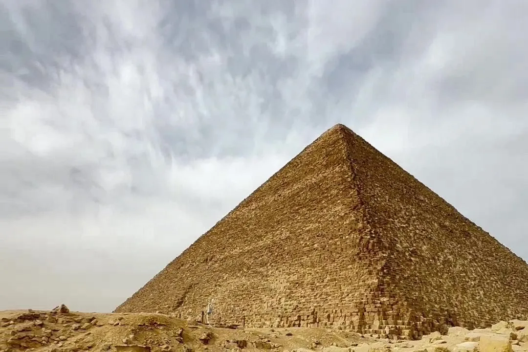 The Great Pyramid of Giza under a streaked cloudy sky, rocky ground in the foreground